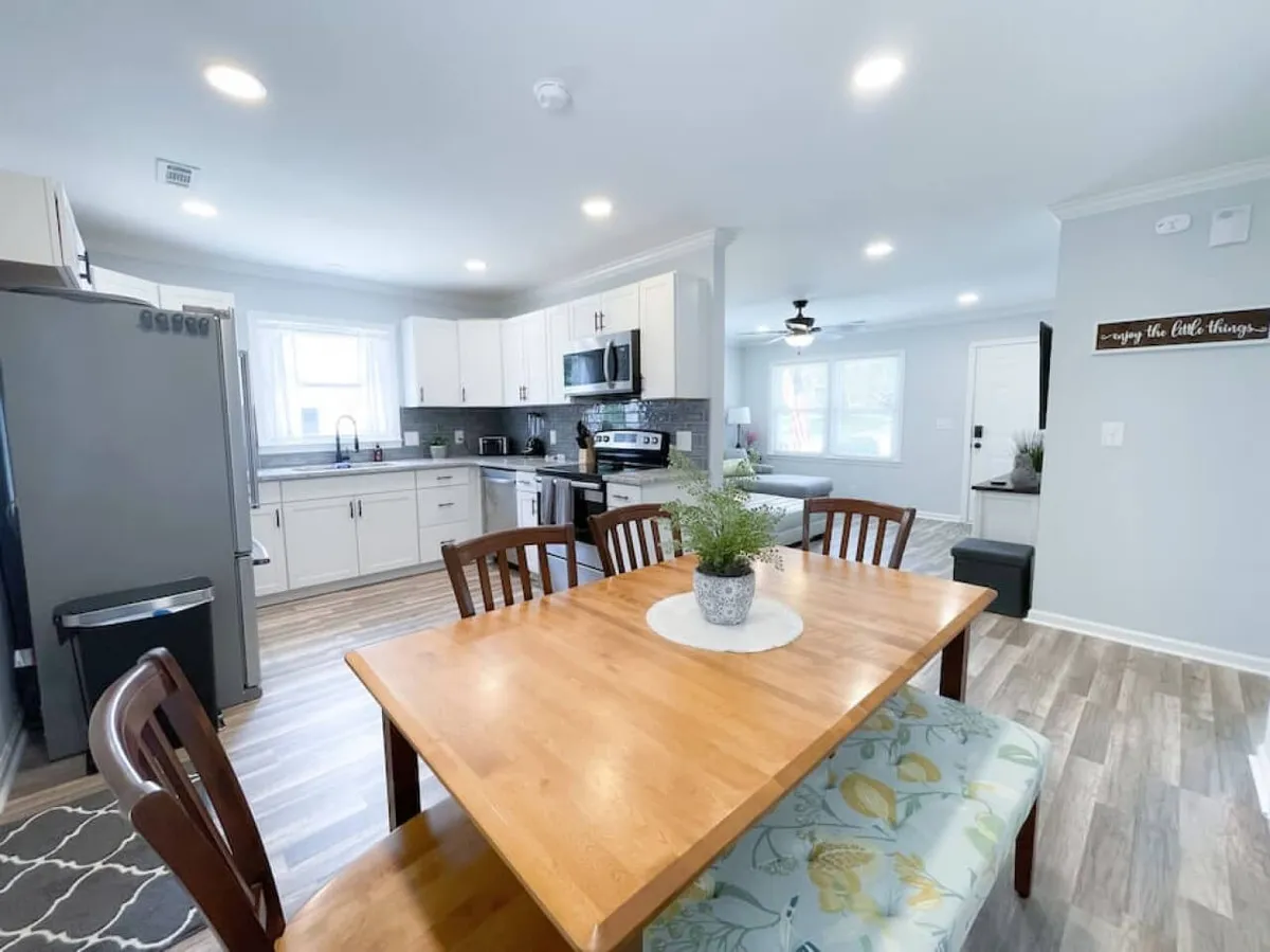 This image offers a wider perspective on the open-concept layout, connecting the kitchen, dining, and living areas. The dining table, decorative centerpiece, and visible kitchen appliances highlight the seamless flow between spaces and encourage group interaction.