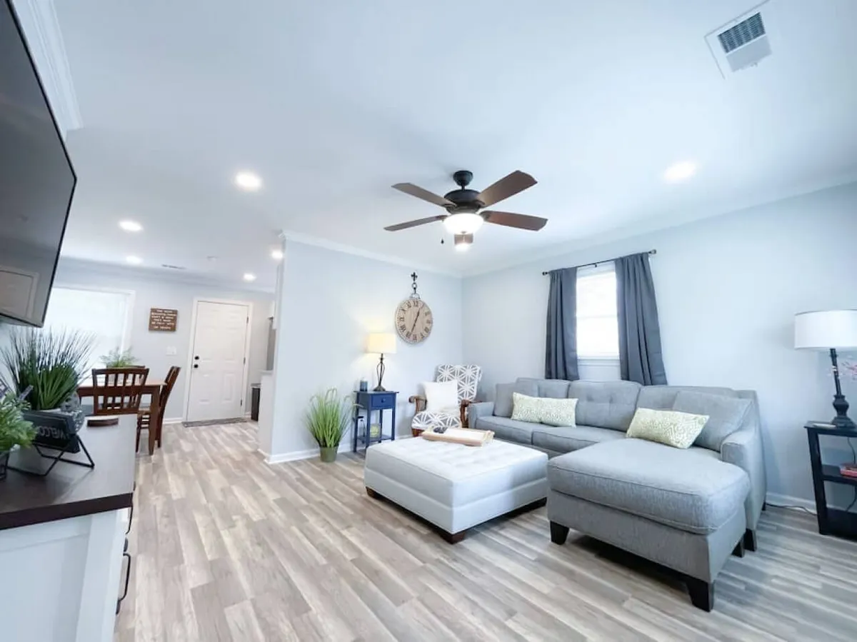 A welcoming, thoughtfully decorated living and dining space with a plush sofa, inviting coffee table, modern ceiling fan, and a spacious dining table. The room is bathed in soft light, radiating comfort and warmth, perfect for relaxing, socializing, or enjoying a cozy evening in.