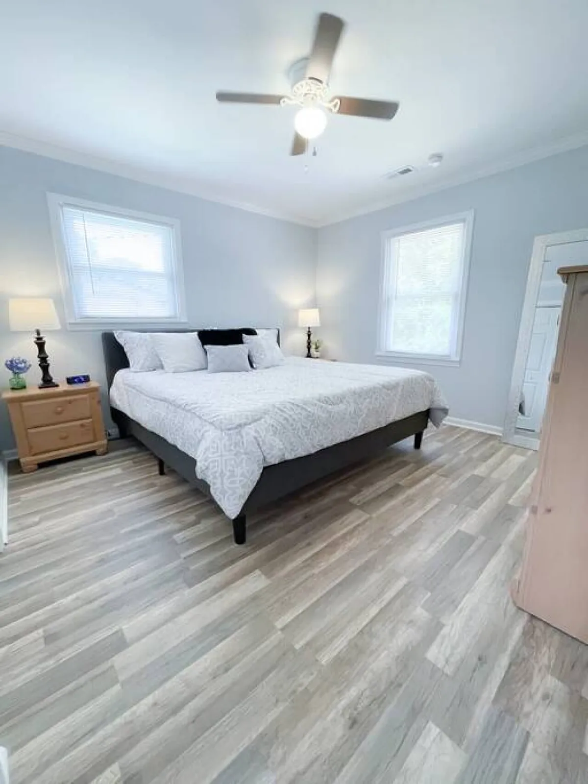 A serene bedroom featuring a large, inviting king bed adorned with decorative pillows, flanked by nightstands with lamps, and bathed in ample natural light from generous windows. The room exudes tranquility and comfort, perfect for restful sleep and morning relaxation.