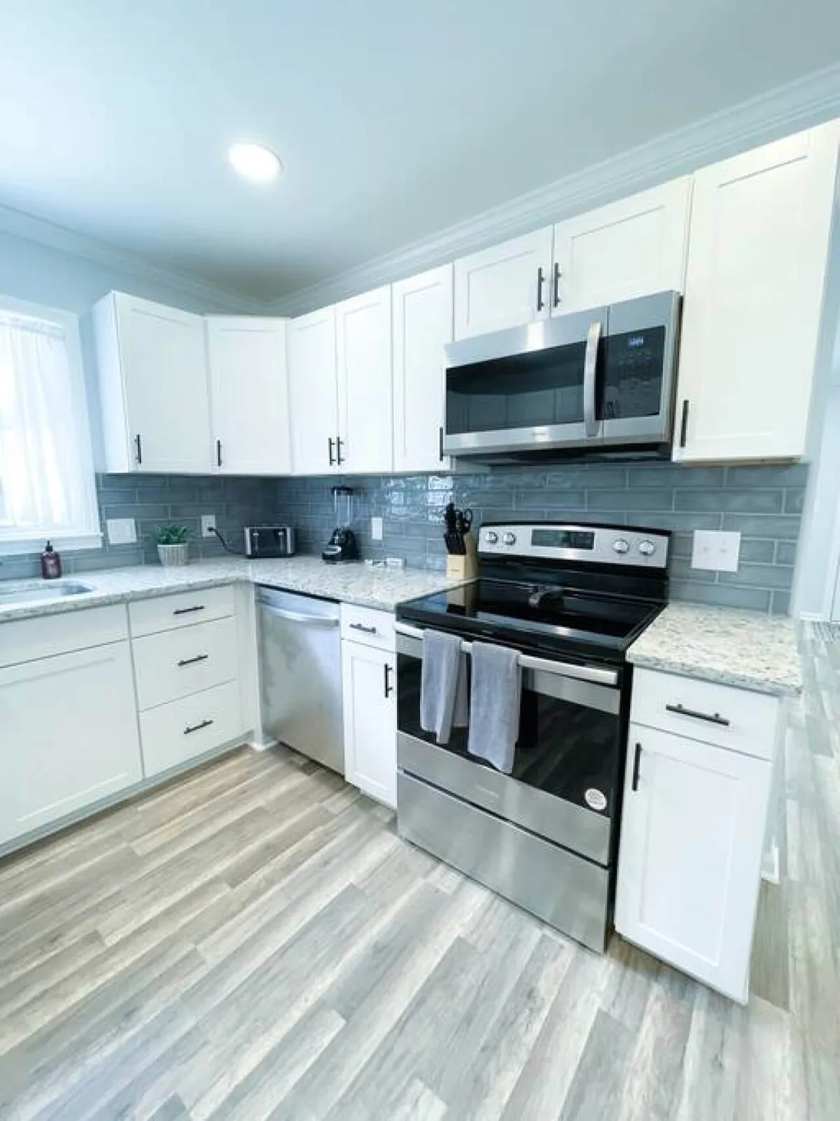 A welcoming kitchen scene showcasing stainless steel appliances, granite countertops, white cabinetry, and a classic subway tile backsplash. The spacious layout suggests functionality and is ideal for preparing large meals or hosting guests. The cabinetry and counters appear well-stocked, hinting at included essentials and cookware.