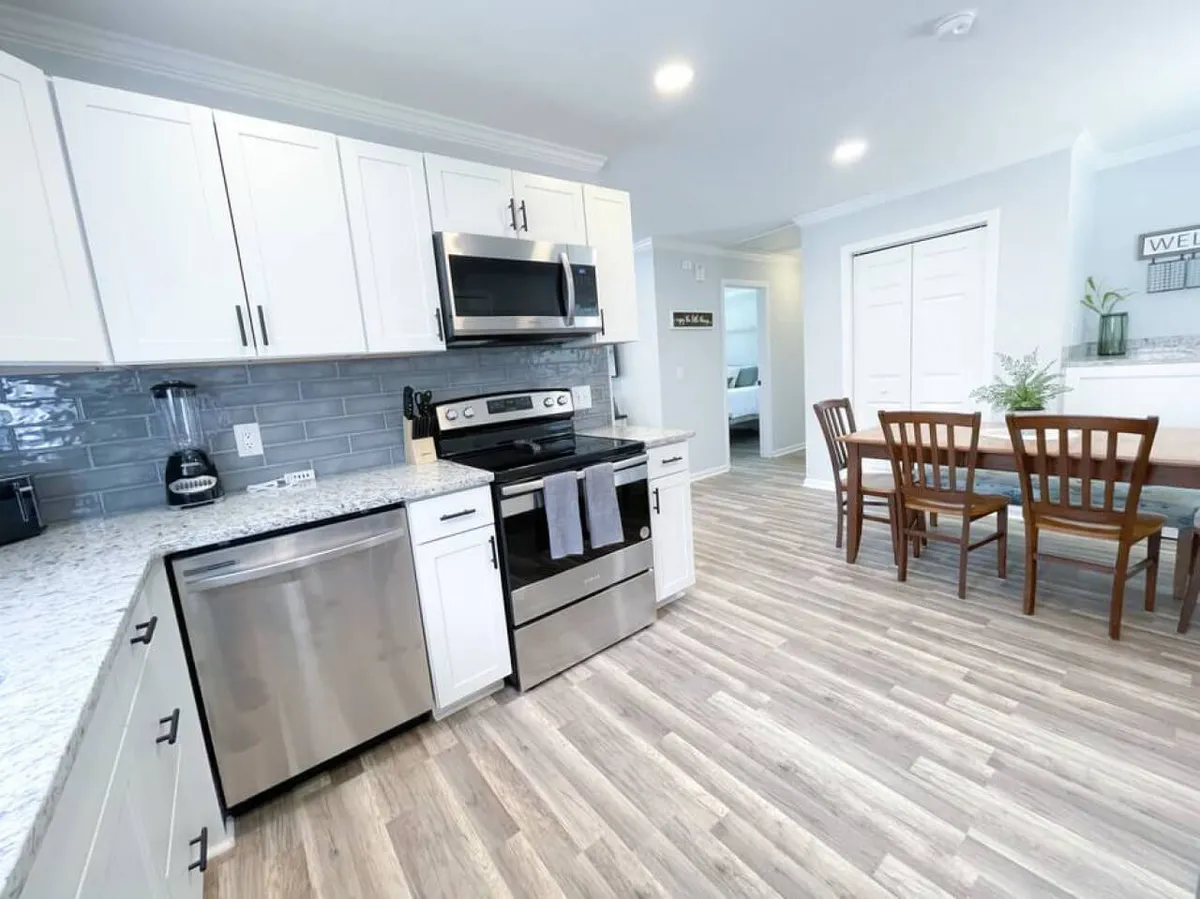 This image features a modern kitchen with stainless steel appliances, a granite countertop, and a wooden dining table. The appliances are prominent, including a refrigerator, oven, and microwave, while the countertop provides ample space for meal prep. The scene conveys a warm and inviting atmosphere perfect for cooking and entertaining.