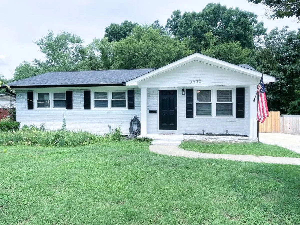 A welcoming exterior shot of the home features a white brick facade, black shutters, a classic front door adorned with an American flag, and a well-kept lawn. The porch and outdoor space are visible, hinting at opportunities to enjoy the neighborhood atmosphere.
